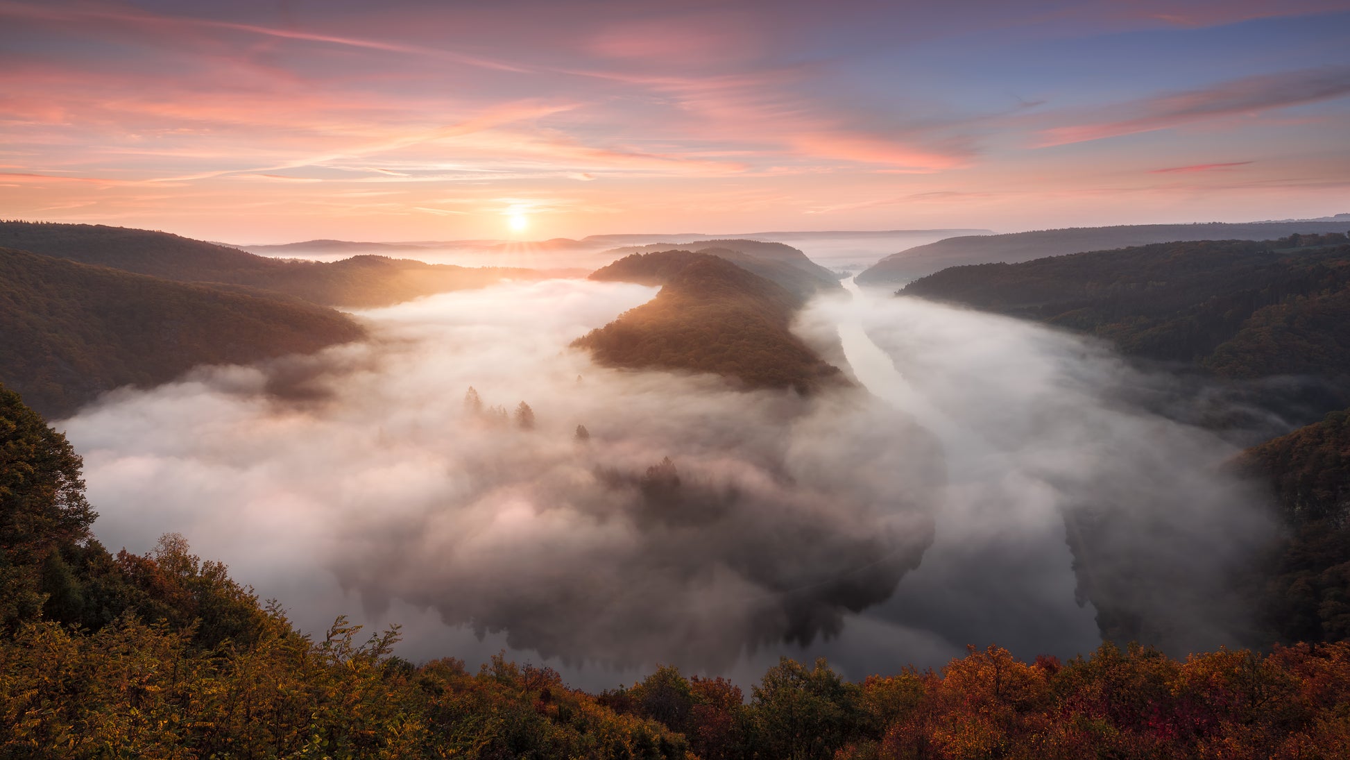 Image Title: The foggy Loop Photographer: Marcus Danz Location: Mettlach, Germany Image description: Mysterious morning fog drifts silently through Mettlach’s Saar loop, partly lit by the warm light of the rising sun. High quality Fine Art print up to 36 inch / around 90 centimeters on Hahnemühle paper available.